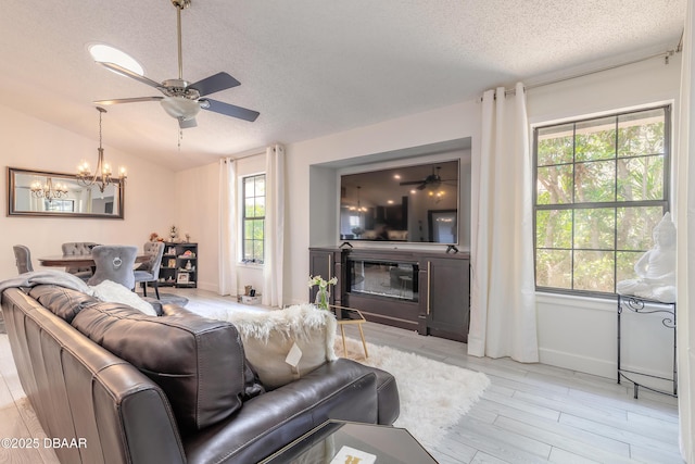 living area featuring a glass covered fireplace, ceiling fan with notable chandelier, a textured ceiling, and vaulted ceiling