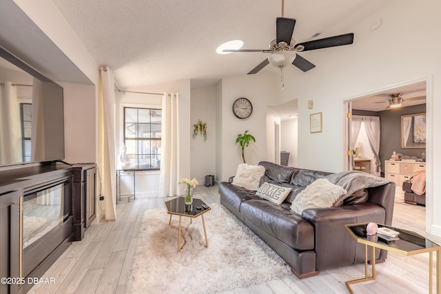 living room featuring vaulted ceiling, a ceiling fan, light wood-type flooring, and a textured ceiling