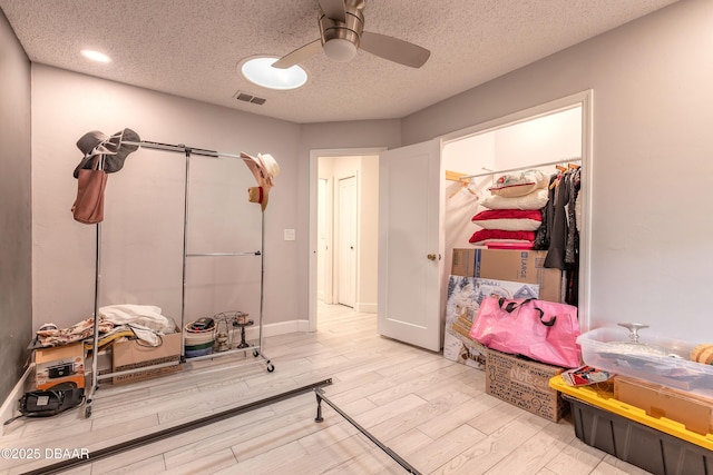 workout area with a ceiling fan, baseboards, wood finished floors, visible vents, and a textured ceiling