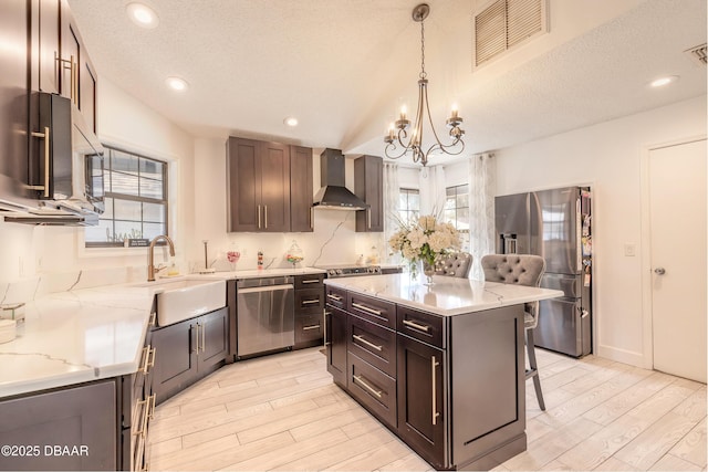 kitchen featuring visible vents, a kitchen breakfast bar, stainless steel appliances, an inviting chandelier, and wall chimney range hood