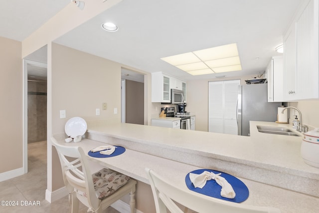 kitchen with stainless steel appliances, white cabinets, kitchen peninsula, sink, and light tile patterned floors