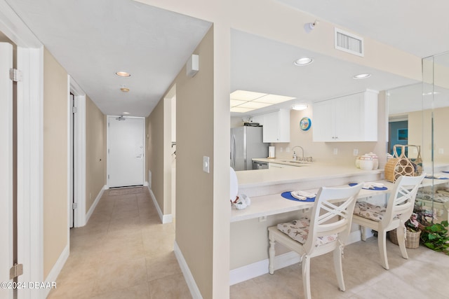 kitchen with stainless steel refrigerator, sink, kitchen peninsula, light tile patterned floors, and white cabinets