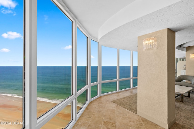 unfurnished sunroom featuring a view of the beach and a water view