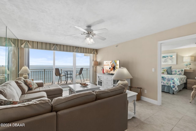 tiled living room featuring a wealth of natural light, ceiling fan, and a water view