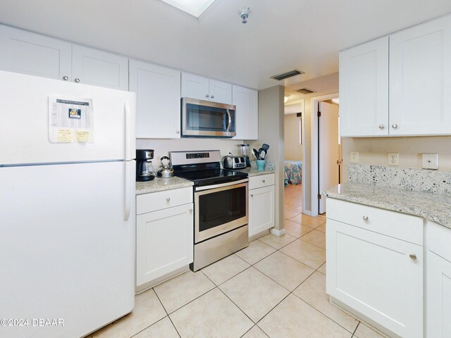 kitchen with light stone counters, white cabinets, light tile patterned floors, and stainless steel appliances