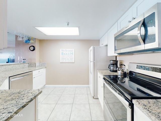 kitchen with light stone counters, white cabinets, light tile patterned floors, a skylight, and appliances with stainless steel finishes