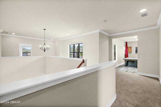 hall with a chandelier, light colored carpet, ornamental molding, and plenty of natural light