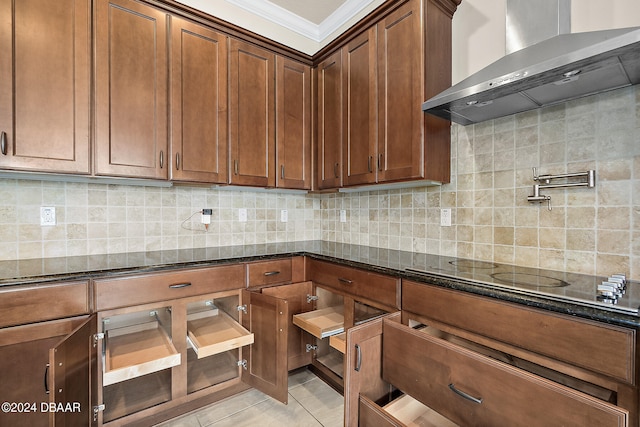 kitchen with wall chimney exhaust hood, tasteful backsplash, crown molding, stovetop, and dark stone countertops