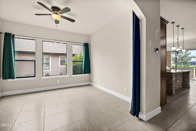 tiled spare room with a wealth of natural light and ceiling fan with notable chandelier