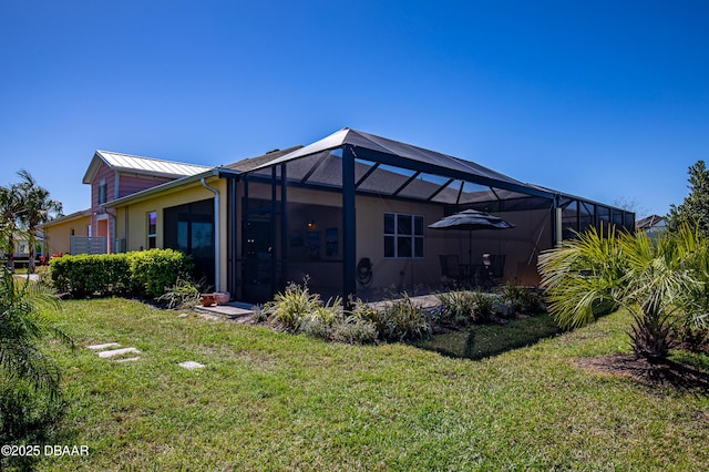 back of property with a standing seam roof, metal roof, a lawn, and glass enclosure