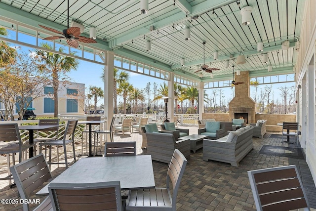 view of patio / terrace featuring ceiling fan, outdoor dining space, and an outdoor living space with a fireplace