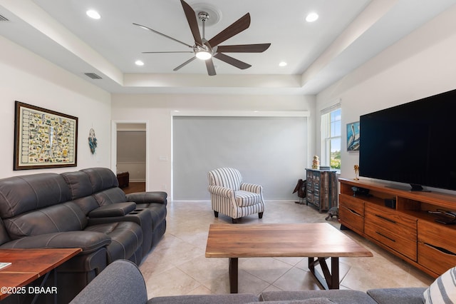 living area with ceiling fan, a tray ceiling, light tile patterned floors, and visible vents