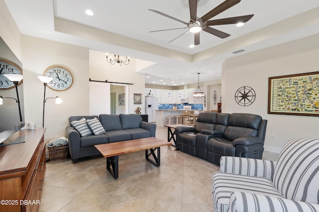 living area featuring a barn door, visible vents, a raised ceiling, and a ceiling fan