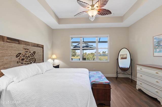 bedroom with a ceiling fan, baseboards, a tray ceiling, and dark wood-type flooring