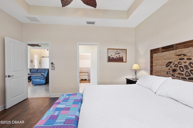 bedroom featuring baseboards, visible vents, ensuite bath, and wood finished floors