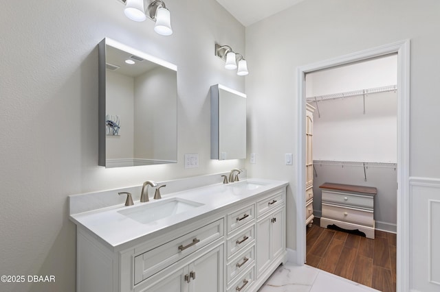 full bath with double vanity, wood finished floors, a spacious closet, and a sink