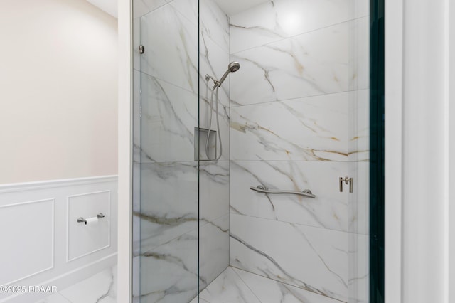 bathroom featuring a marble finish shower, a decorative wall, and wainscoting