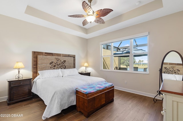 bedroom with wood finished floors, a raised ceiling, and baseboards