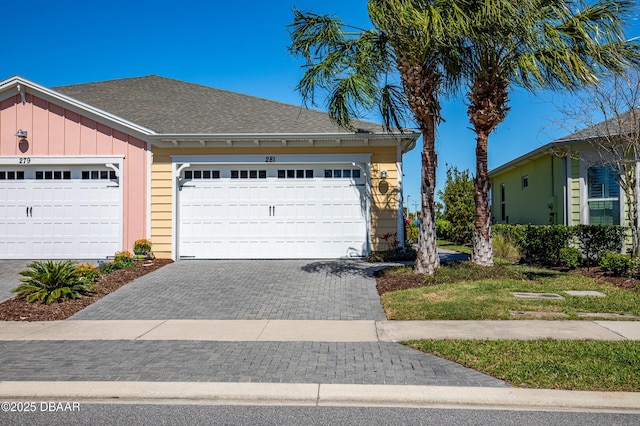 view of front of property featuring an attached garage, a shingled roof, decorative driveway, and board and batten siding