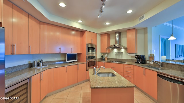 kitchen with light stone counters, a center island with sink, appliances with stainless steel finishes, sink, and wall chimney exhaust hood