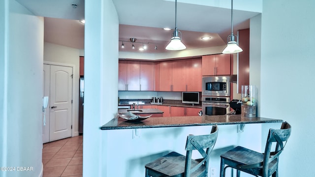 kitchen with dark stone counters, pendant lighting, appliances with stainless steel finishes, and kitchen peninsula