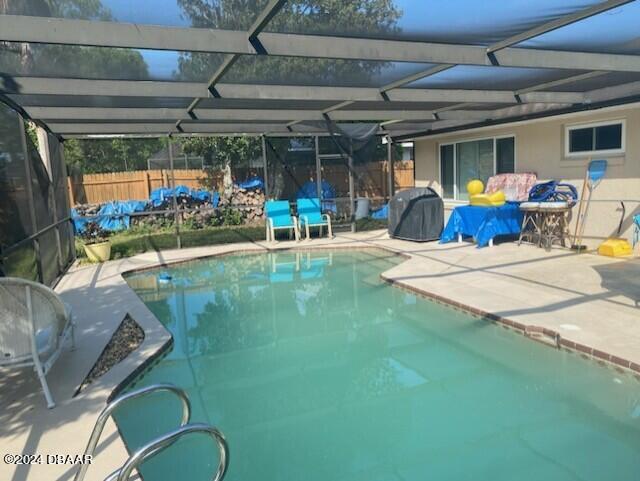 view of swimming pool with glass enclosure, a patio area, and a grill