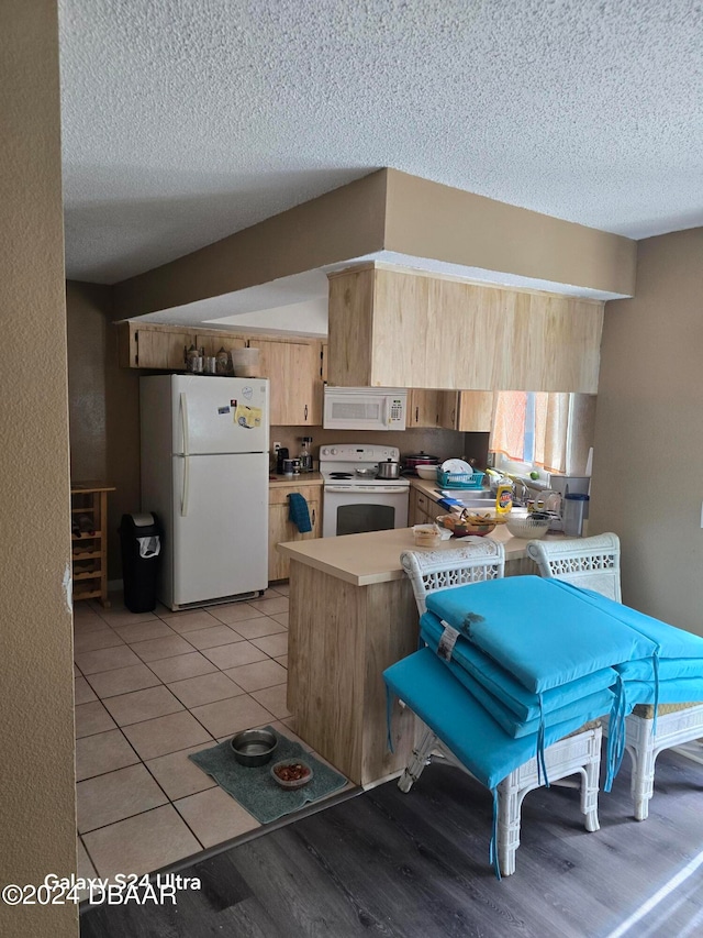 kitchen with light brown cabinets, kitchen peninsula, a textured ceiling, and white appliances