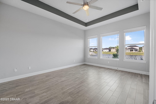 spare room with a ceiling fan, a raised ceiling, baseboards, and wood finished floors