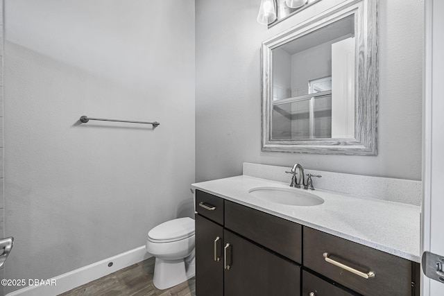 bathroom with a shower stall, baseboards, toilet, wood finished floors, and vanity