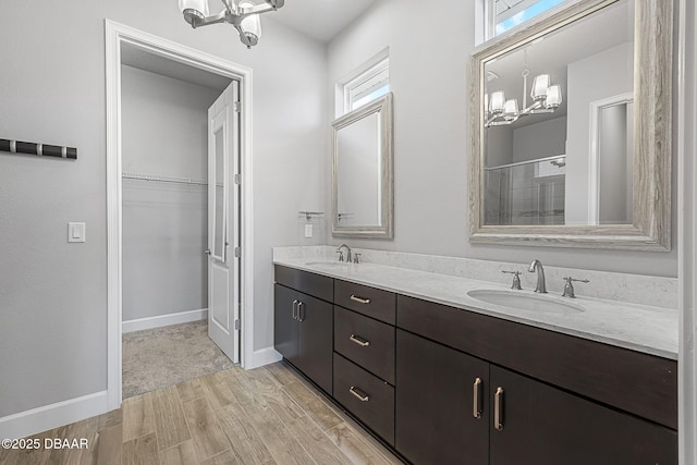 full bath featuring a walk in closet, a notable chandelier, wood finished floors, and a sink