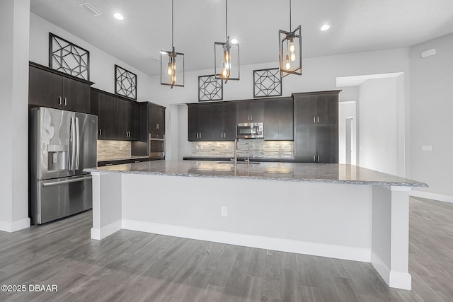 kitchen featuring visible vents, a large island with sink, wood finished floors, stainless steel appliances, and a sink