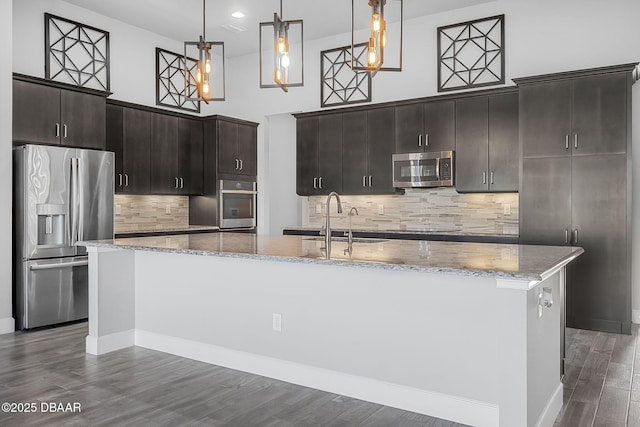 kitchen with a kitchen island with sink, a sink, dark wood finished floors, stainless steel appliances, and a towering ceiling