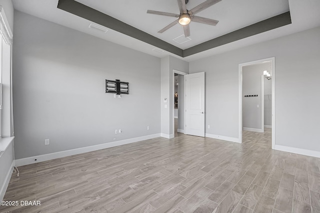 unfurnished bedroom featuring visible vents, light wood-style flooring, baseboards, and a tray ceiling