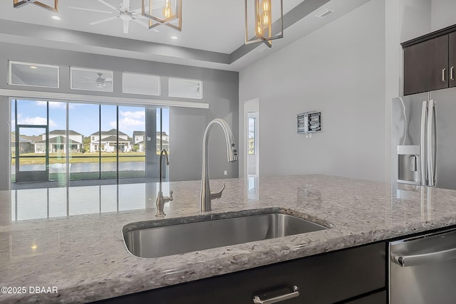 kitchen with light stone counters, stainless steel appliances, dark brown cabinets, and a sink