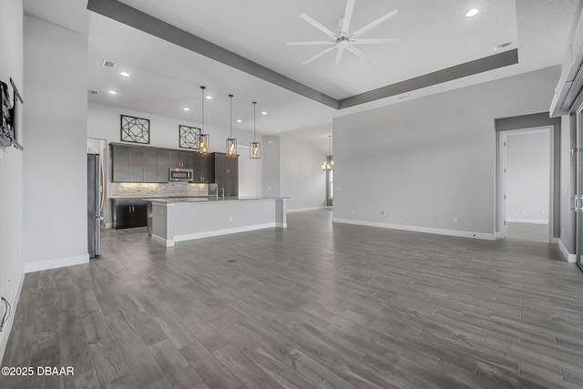 unfurnished living room with ceiling fan with notable chandelier, recessed lighting, baseboards, and dark wood-style flooring