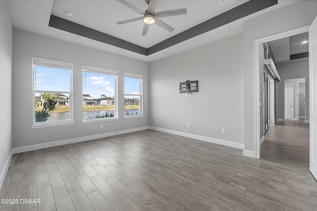 spare room with visible vents, baseboards, a tray ceiling, and wood finished floors