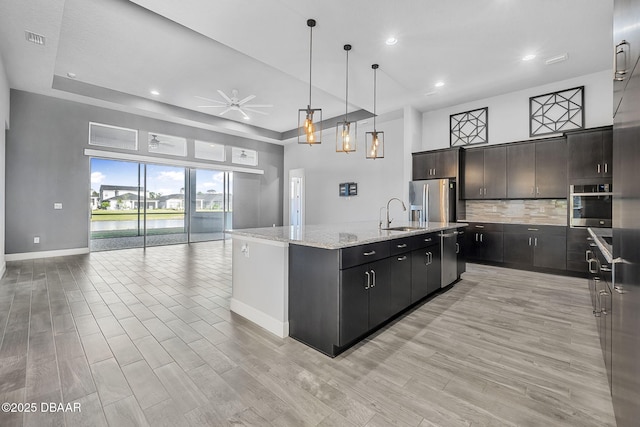 kitchen with open floor plan, a center island with sink, light wood-style flooring, appliances with stainless steel finishes, and a sink