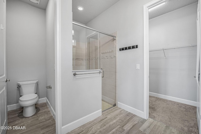 bathroom featuring a shower stall, a walk in closet, baseboards, toilet, and wood finished floors