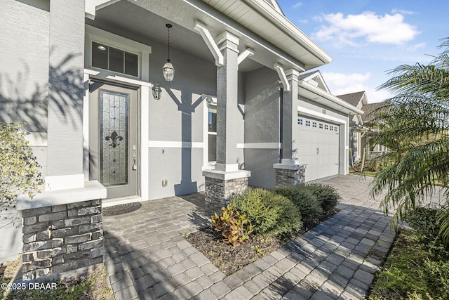 doorway to property with decorative driveway, a porch, and an attached garage