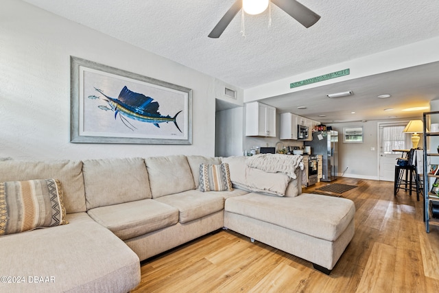 living room with ceiling fan, a textured ceiling, and light wood-type flooring