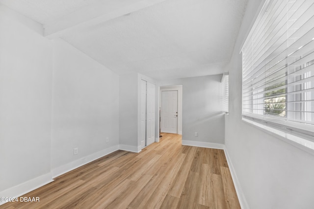 spare room featuring light hardwood / wood-style flooring, a textured ceiling, and beam ceiling