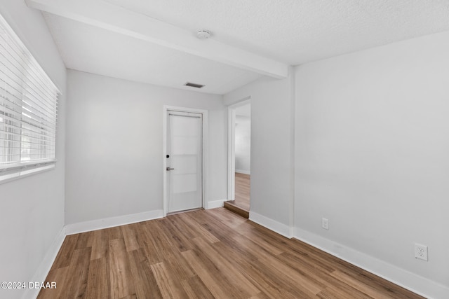 empty room featuring a textured ceiling, hardwood / wood-style flooring, and beam ceiling