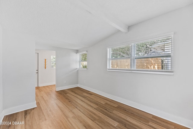 spare room featuring light wood-type flooring, vaulted ceiling with beams, a healthy amount of sunlight, and a textured ceiling