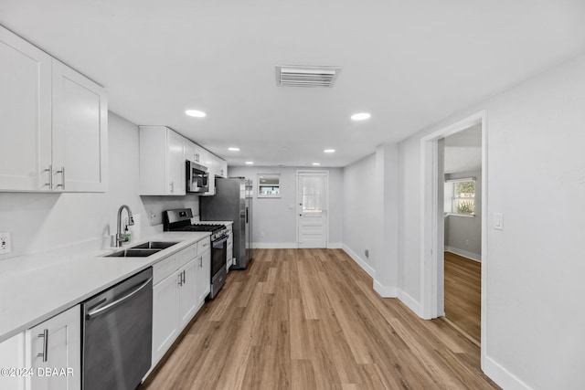 kitchen featuring stainless steel appliances, white cabinets, sink, and light wood-type flooring