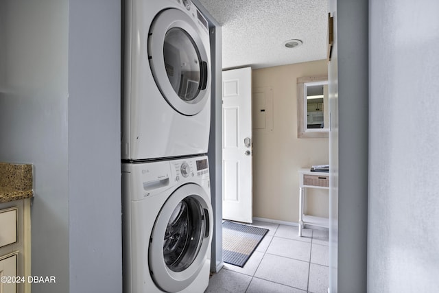 laundry room with a textured ceiling, light tile patterned floors, and stacked washer and clothes dryer