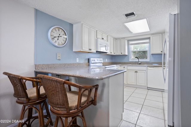 kitchen with a textured ceiling, white appliances, kitchen peninsula, and a breakfast bar area