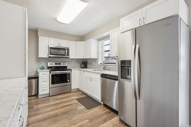 kitchen with appliances with stainless steel finishes, tasteful backsplash, white cabinetry, sink, and light hardwood / wood-style floors