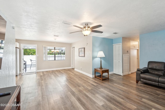 living room featuring hardwood / wood-style flooring, ceiling fan with notable chandelier, and a textured ceiling