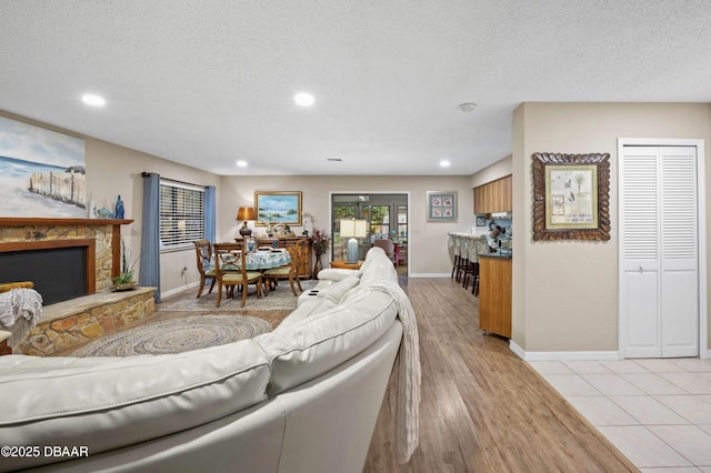 living room featuring a stone fireplace, light tile patterned floors, and a textured ceiling