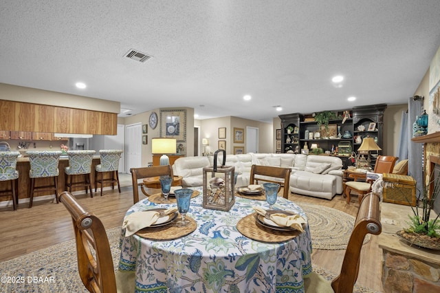 dining area featuring light wood-type flooring, a textured ceiling, and a fireplace